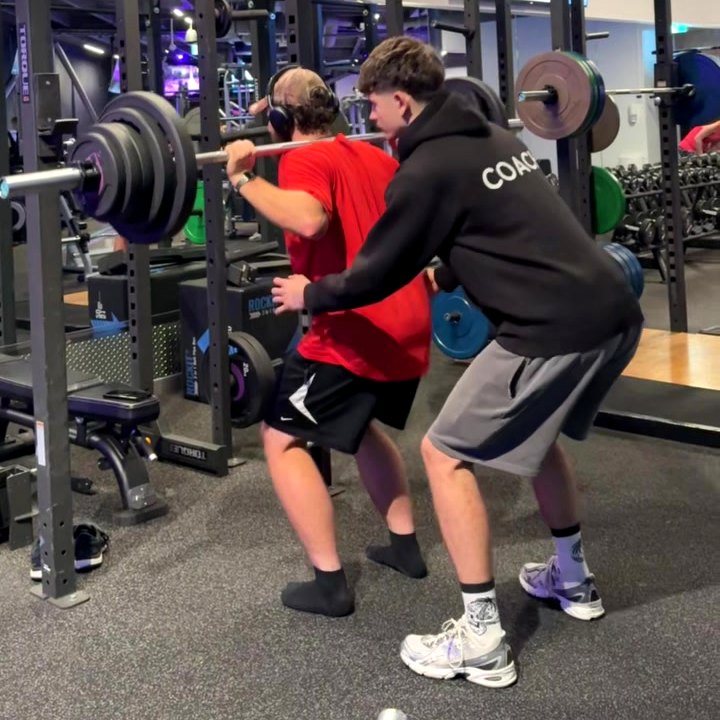 Jack Brookes spotting a heavy barbell squat in the weights room at Anytime Fitness Silverdale.